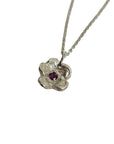 Silver necklace with a floral pendant and red gemstone on a light gray background