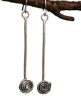 Silver spiral earrings hanging from a branch with a natural background irish jewellery