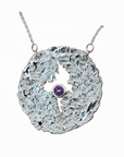 Silver necklace with a textured pendant featuring a blue gemstone on a white background