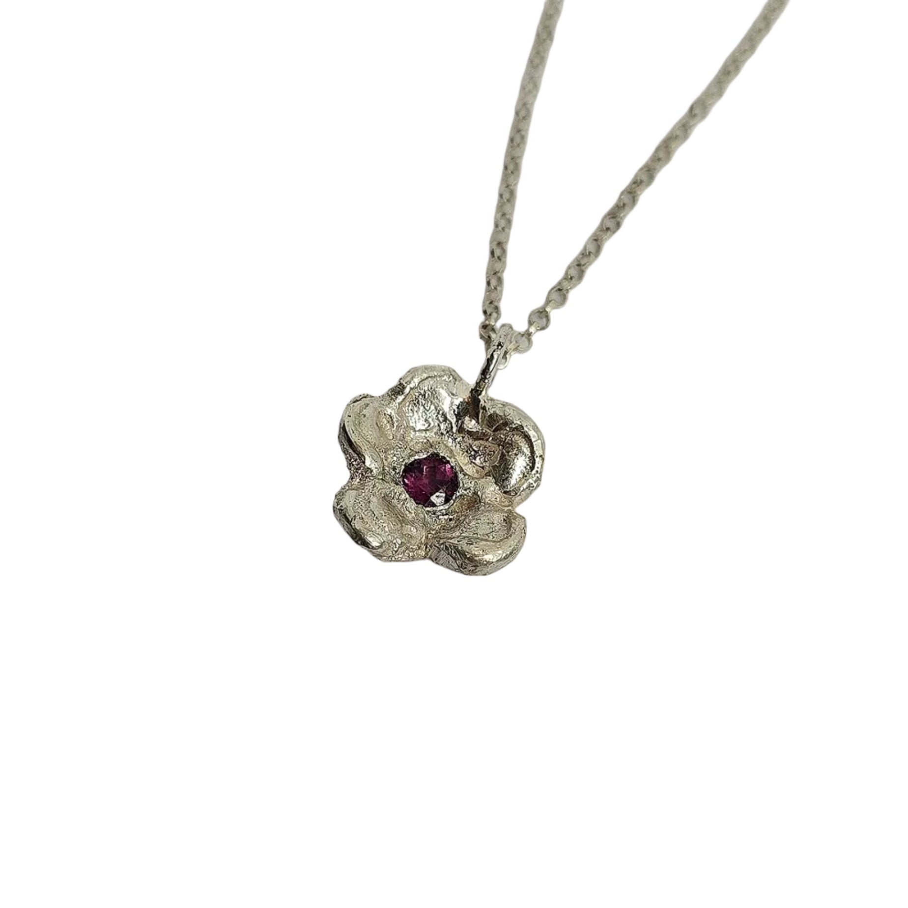 Silver necklace with a floral pendant and red gemstone on a light gray background